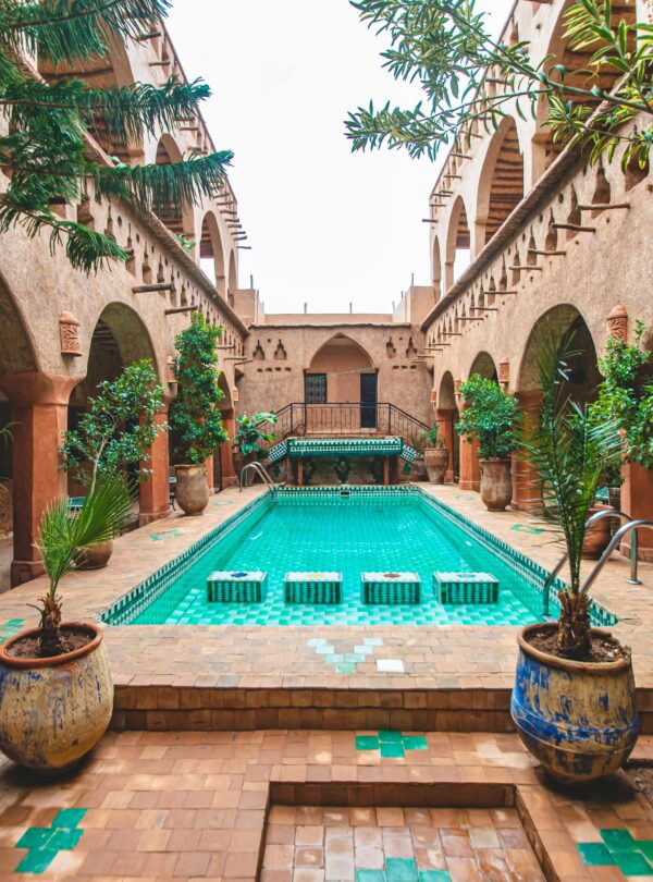 Charming pool courtyard of a traditional riad in Ouarzazate, Morocco, with lush plants and intricate architecture.
